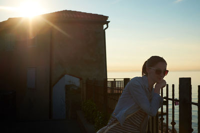 Young woman in sunglasses standing by sea on sunny day