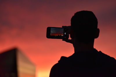 Silhouette man photographing against sky during sunset