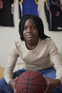 Portrait of teenage girl holding basketball while sitting at home
