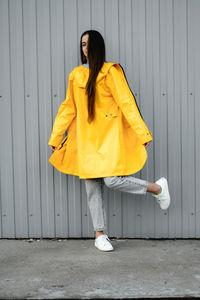 Girl in a yellow raincoat and gray jeans stands on a gray background. youth subculture