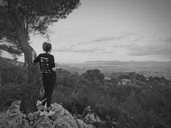 Rear view of man standing on rock against sky