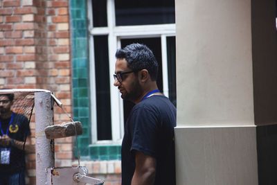 Side view of young man standing against window