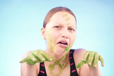 Close-up portrait of young woman with painted hands against blue background