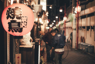 Text on illuminated lantern hanging at market in city during night