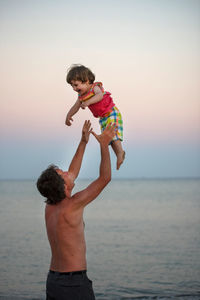 Father and son standing on beach against clear sky