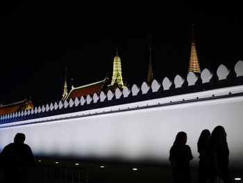 People at illuminated temple building against sky at night