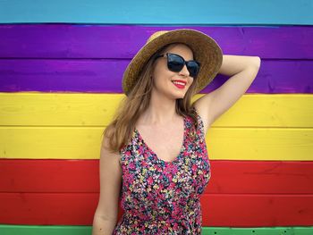 Smiling young woman wearing sunglasses against wall