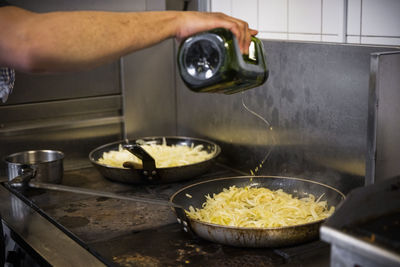 Cropped image of chef pouring oil on food in pan at restaurant kitchen