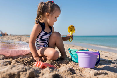 Cute girl sitting on beach by sea against sky