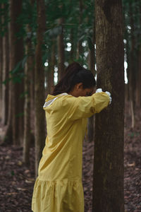 Woman standing by tree trunk in forest