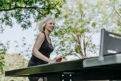 Smiling mature woman playing table tennis in park