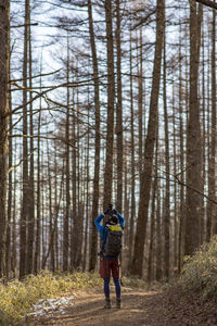 Rear view of backpacker photographing trees in forest