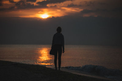 Rear view of silhouette man standing on beach at sunset