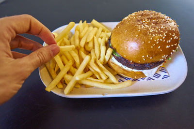 Cropped hand having burger and french fries in bowl on table