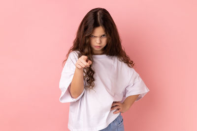 Portrait of young woman standing against pink background