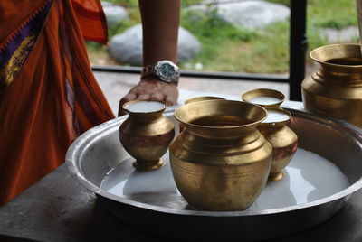 Midsection of man standing by milk in utensils on table at buddhist temple