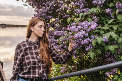 Portrait of beautiful young woman standing by flowering plants