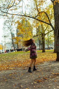 Side view of young woman tossing hair against autumn trees at park