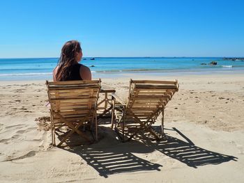 Rear view of woman sitting on beach against clear sky