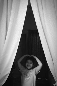 Smiling boy standing amidst curtains at home