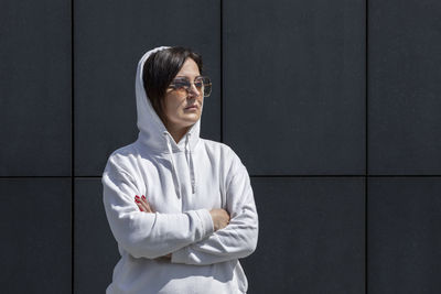 Portrait mature brunette woman with hood on head, wears white hoodie and sunglasses with crossed