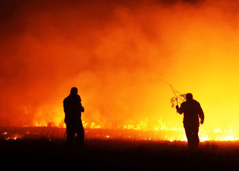 Silhouette firefighters working on burning gassy field