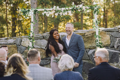 Happy newlywed multiracial couple looking at guest during wedding ceremony