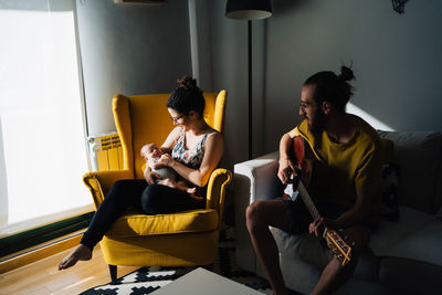 Woman sitting on yellow sofa at home holding her new born baby