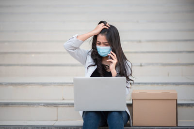 Woman using laptop by box on staircase