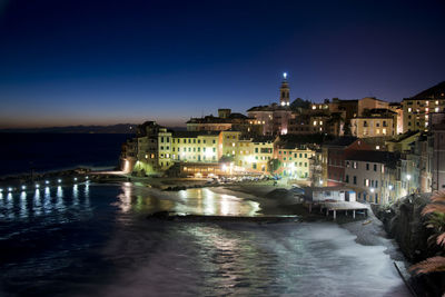 Illuminated buildings by river against sky at night