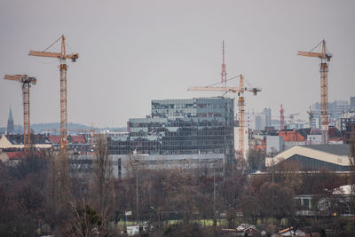 Cranes by buildings against sky in city