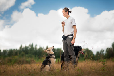 Man training dogs on grassy land against cloudy sky