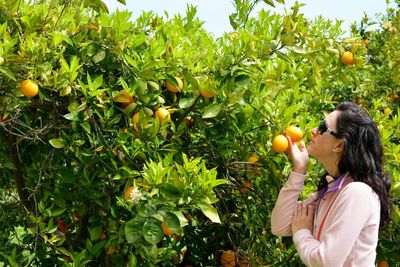 Woman smelling fruit while standing by plant