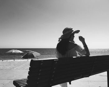 Rear view of woman sitting on bench at promenade against clear sky