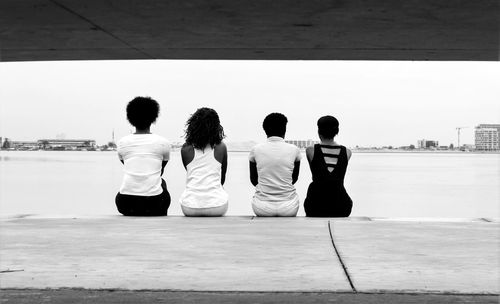 Rear view of friends sitting on jetty against sea