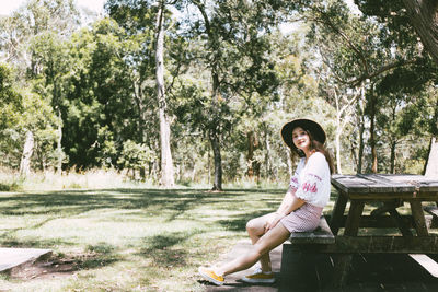 Full length portrait of mid adult woman sitting on picnic table in park