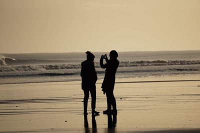 Silhouette people at beach against sky