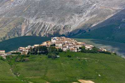 Buildings and mountains in front of green landscape on sunny day at castelluccio