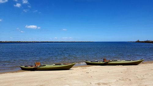 Sailboats moored on beach against blue sky