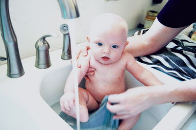 Cropped hands of mother bathing son in sink at bathroom