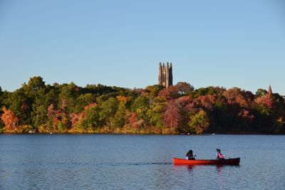 Women canoeing on lake against clear sky during autumn