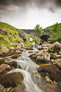 Stream flowing through rocks against sky