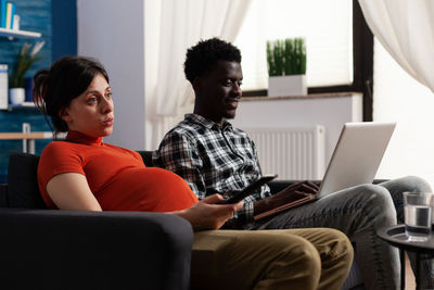 Pregnant woman with man sitting on sofa at home