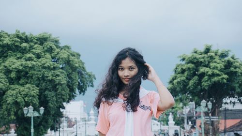 Portrait of young woman standing against trees