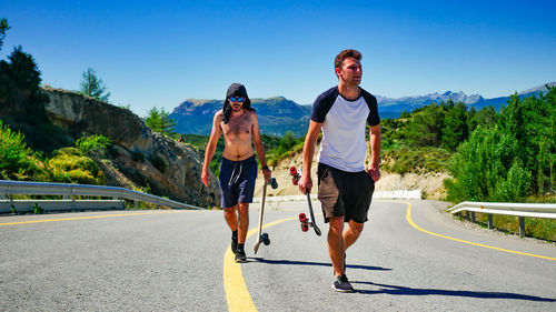 Male friends carrying skateboards on road