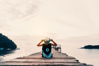 Rear view of girl sitting on pier over sea against sky