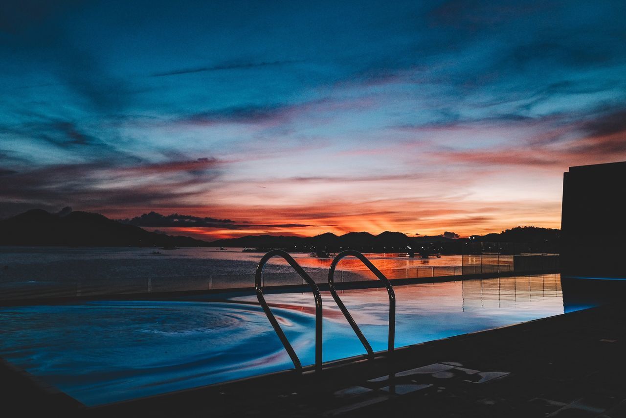 SILHOUETTE SWIMMING POOL AGAINST SKY AT SUNSET