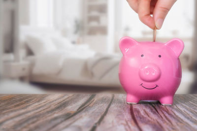 Midsection of man putting coin in piggy bank on table