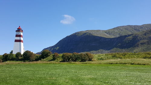 Lighthouse on field by mountain against sky