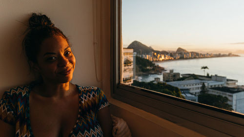 Side view of young woman smiling in front of a window during sunrise